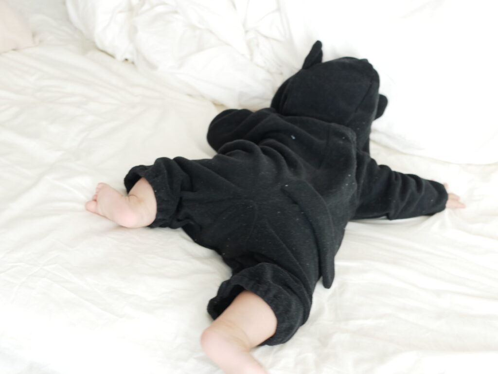 黒猫の着ぐるみを着た赤ちゃんがベッドで寝ている